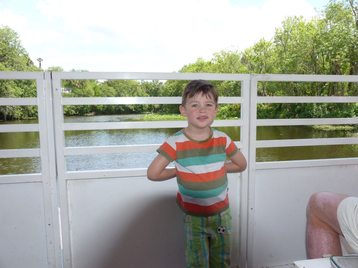 Noah on the deck of the river boat, the tree-lined river behind him