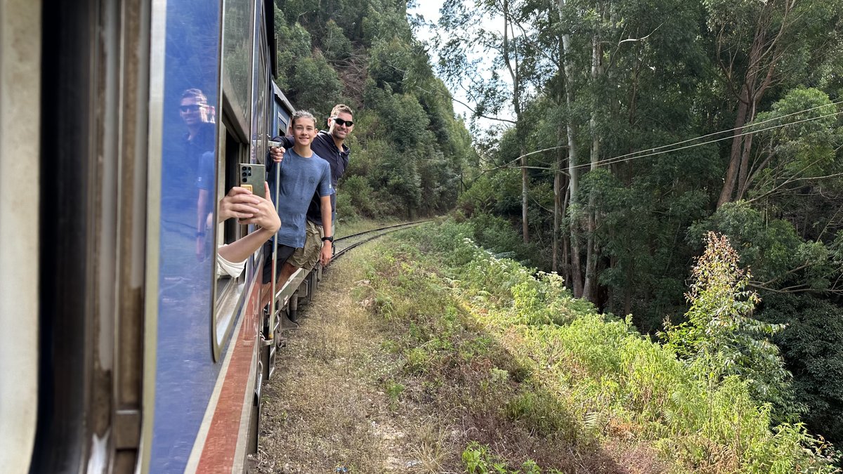 Noah and Jesper leaning out along the side of the blue train as it rounds a bend
